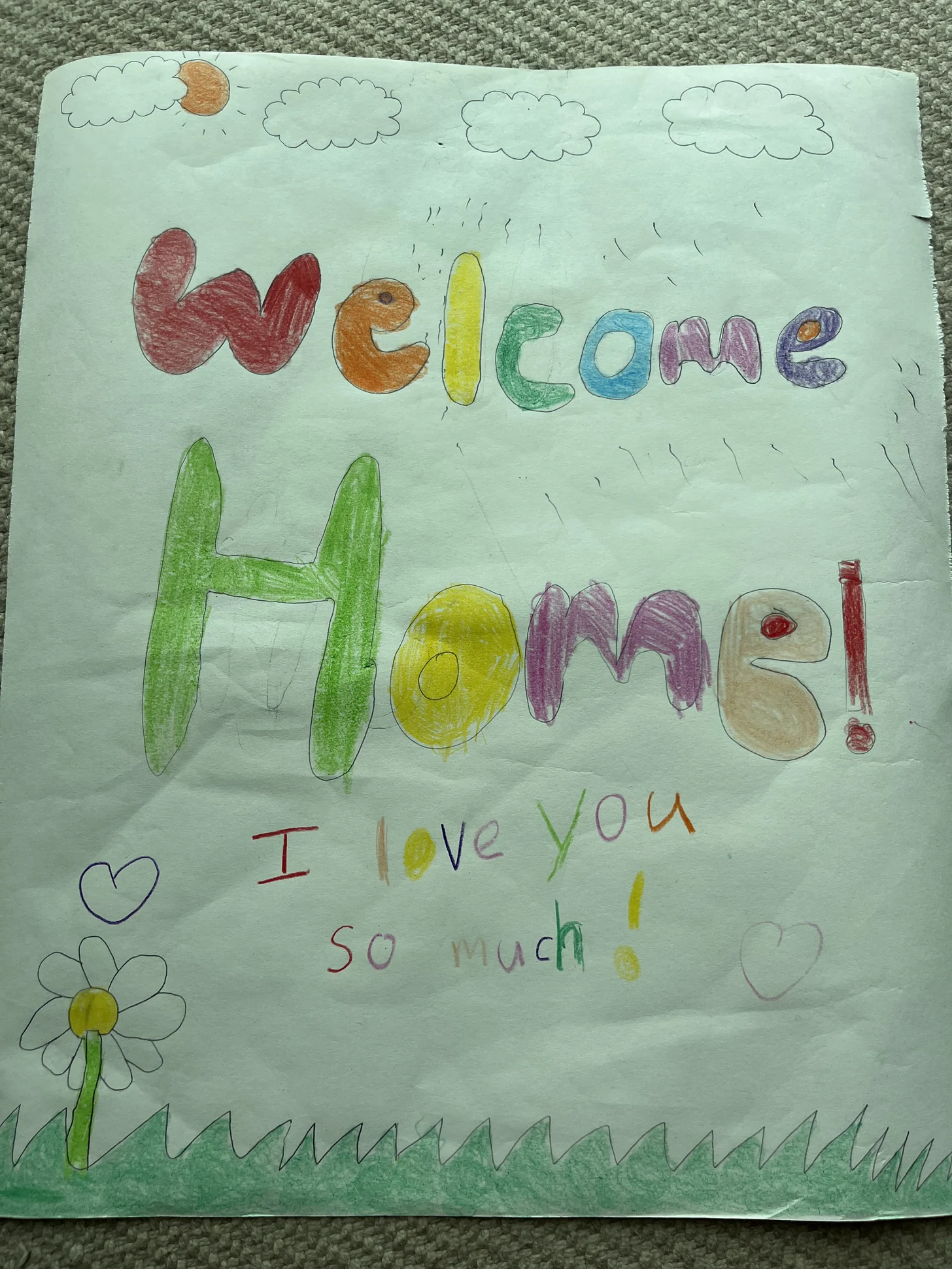 A colorful drawing from the kids reading ‘Welcome Home! I love you so much!’ with clouds, hearts, and a flower.